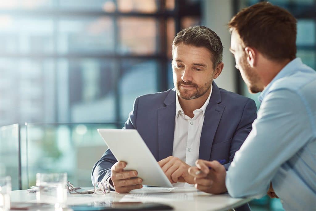 Two men look over business sales documents at a table.