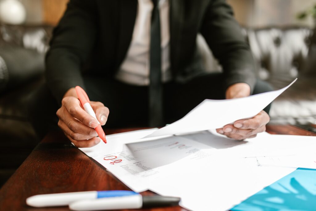 A business broker in a black suit and tie uses a red highlighter to review business financials.